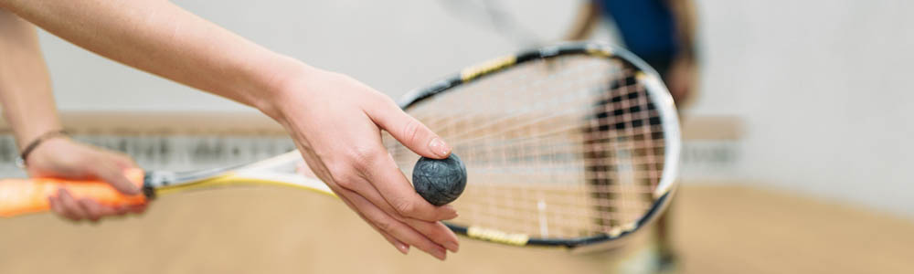 Close-up of woman's hands as she holds a squash ball up to a racquet, preparing to serve on a squash court Close-up of woman's hands as she holds a squash ball up to a racquet, preparing to serve on a squash court